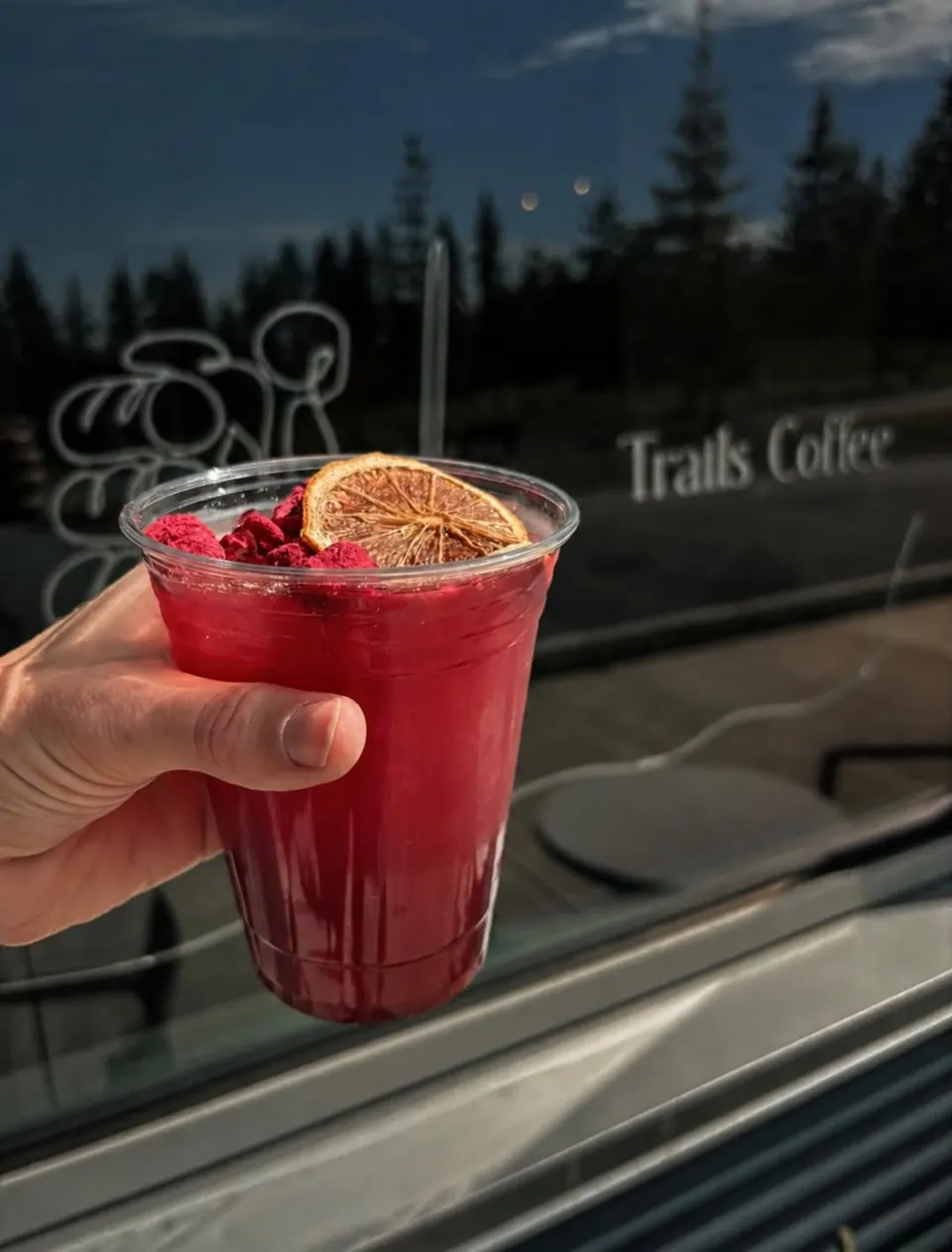 A raspberry lemonade with berries and dried citrus held in front of the Trails Coffee window